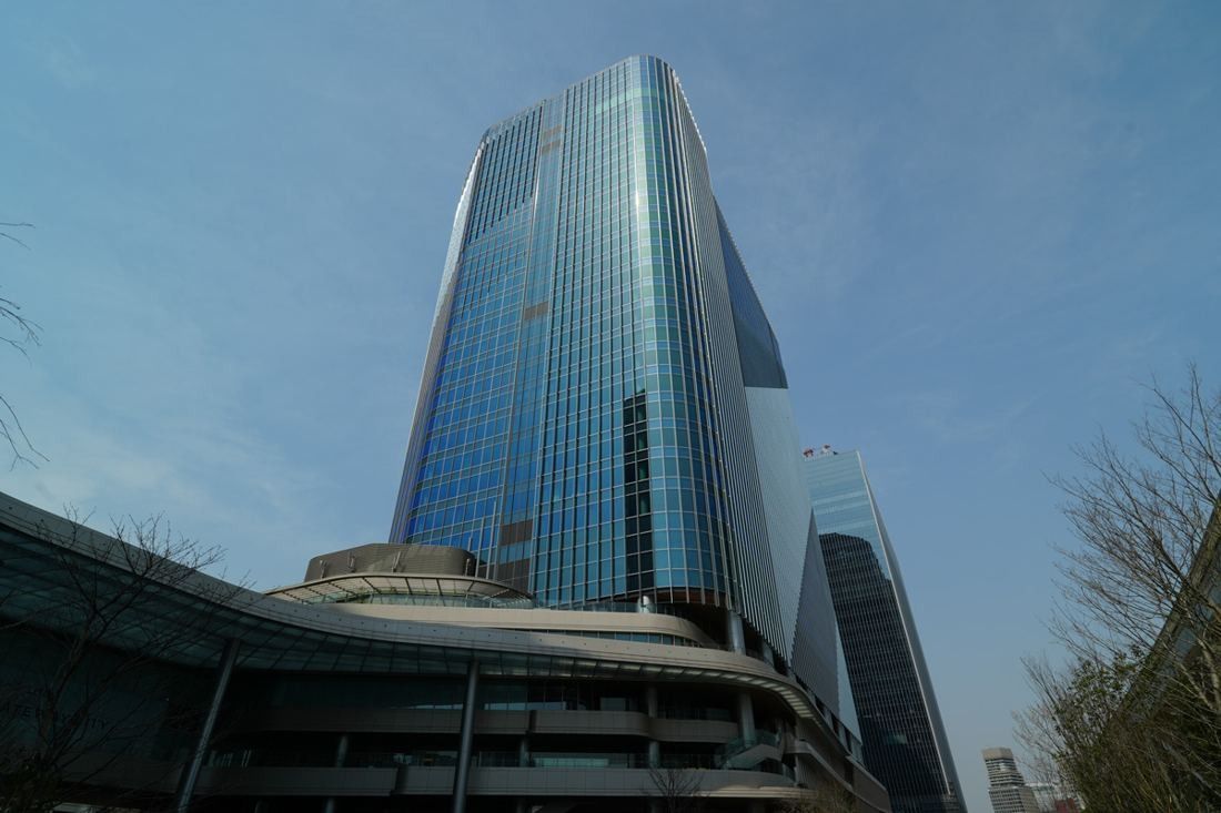 KDDI: Looking up at a glass tower above a curving podium, with another tower behind
