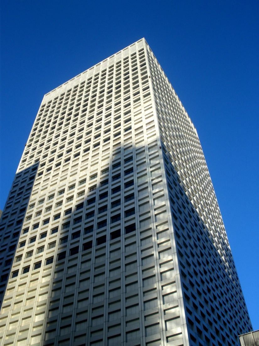 Looking up at a pale grid-facade skyscraper against a deep blue sky