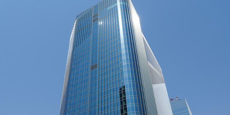 KDDI: The upper part of a blue glass tower against a clear sky