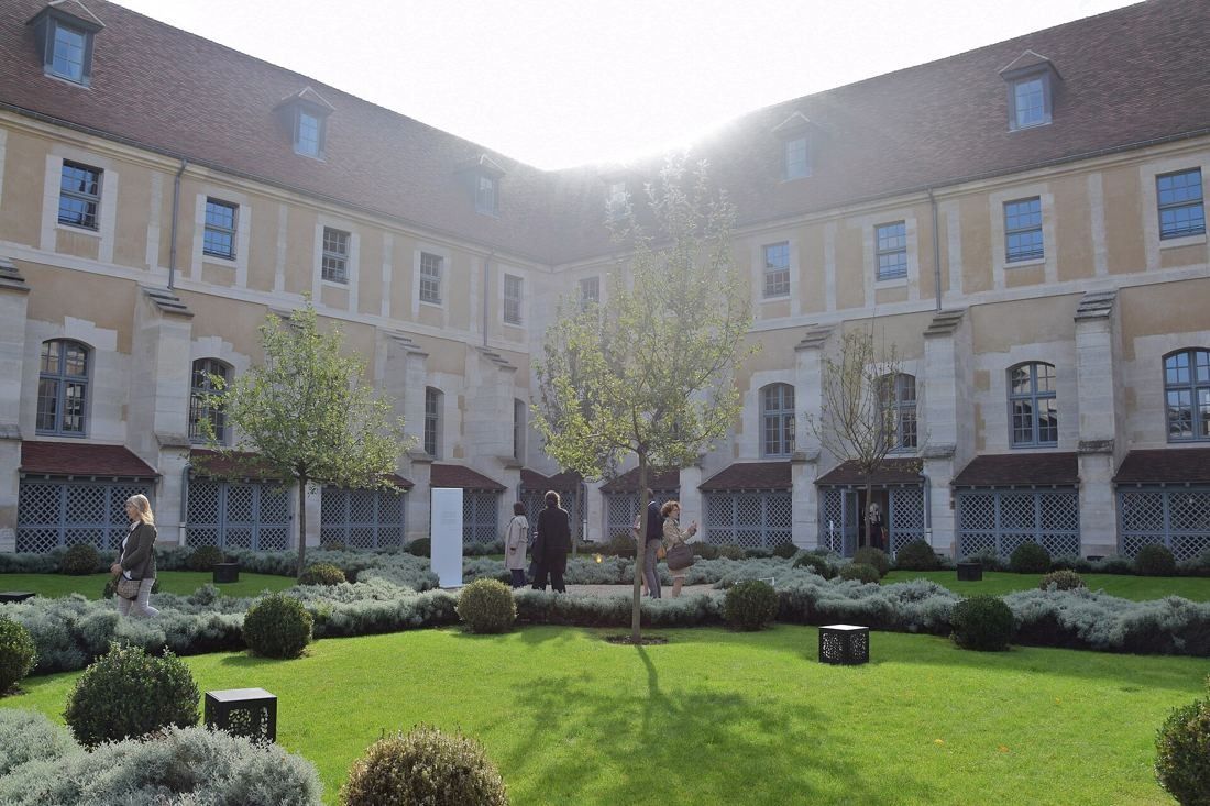 Kering: Backlit courtyard garden enclosed by long stone wings with dormer windows