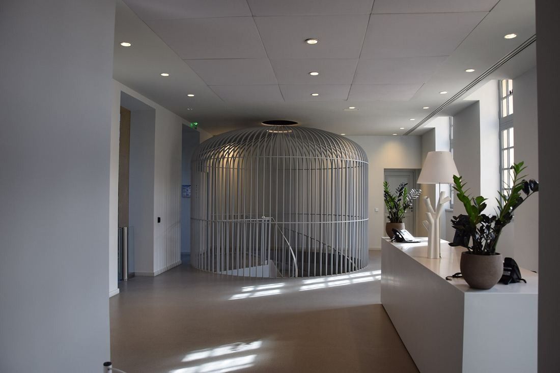 Kering: Bright reception hall with a large white birdcage-shaped structure around a staircase and a white desk with plants