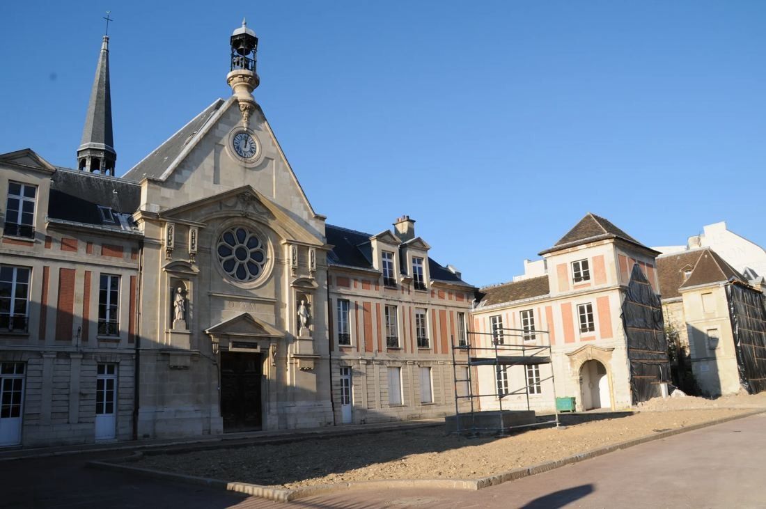 Kering: Chapel facade with rose window flanked by brick-and-stone buildings on a paved courtyard