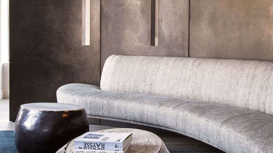 Kering: Close view of a curved pale sofa against a bronze-toned wall with slim light slots