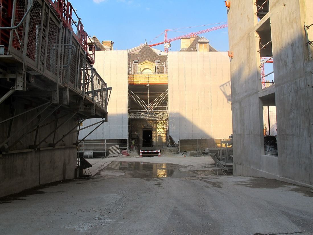 Construction site between concrete structures with the wrapped chapel facade and a crane behind