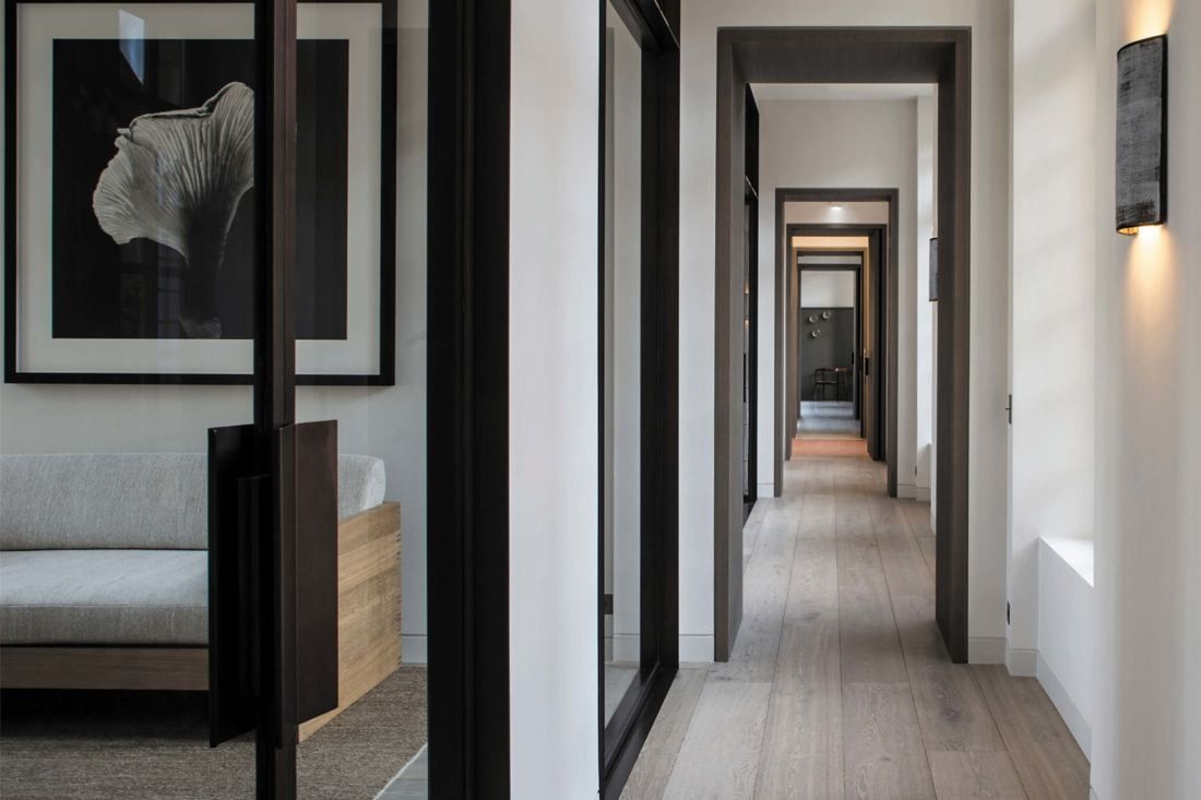 Kering: Corridor with dark-framed glass doors, a framed photograph and a sofa in a side room