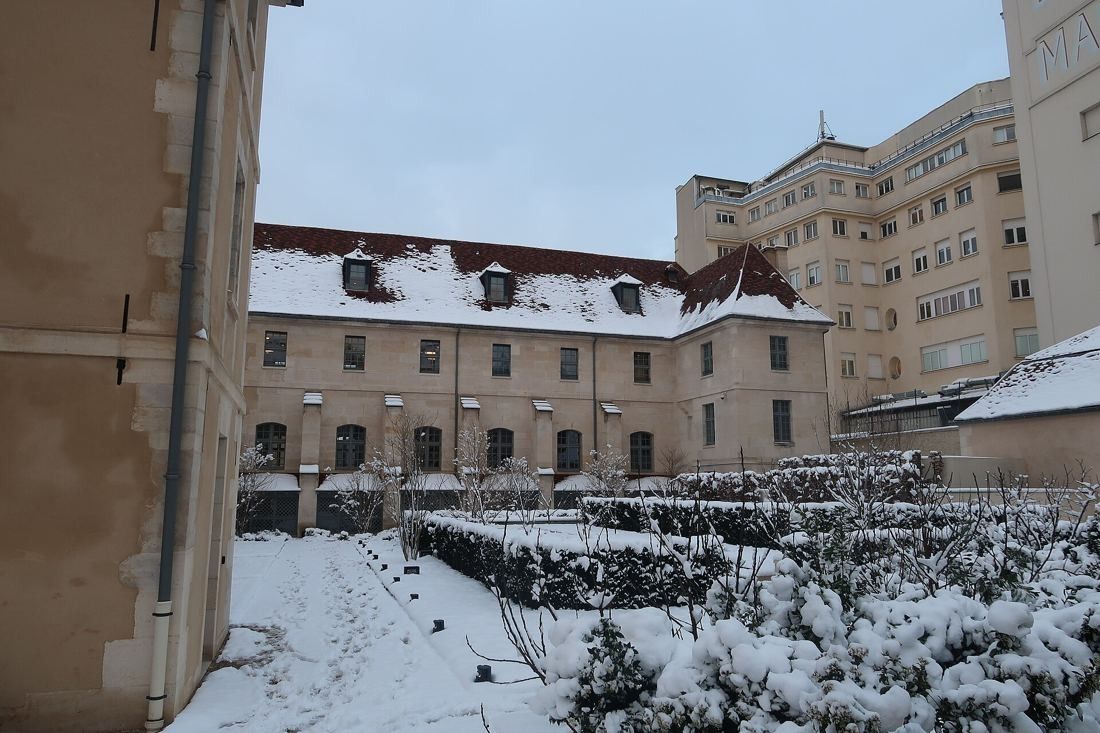 Kering: Courtyard garden covered in snow in front of a stone wing
