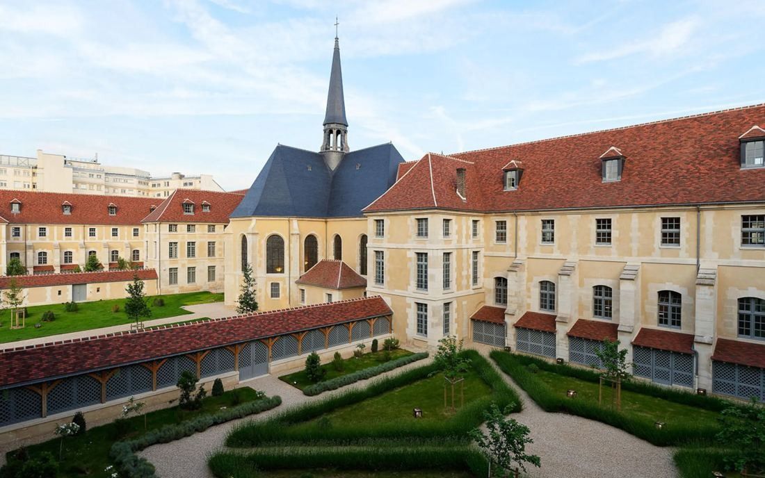 Kering: Formal garden courtyard surrounded by historic wings with red-tiled roofs and a chapel spire