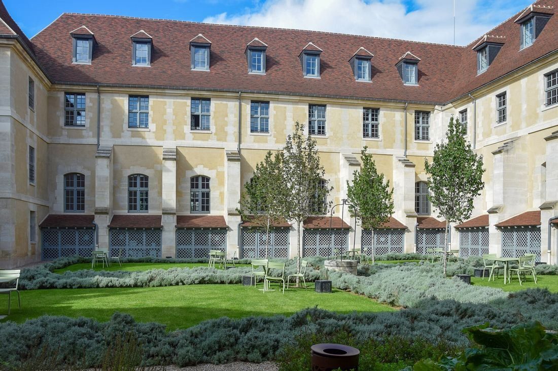 Kering: Garden courtyard with lavender beds and young trees enclosed by a three-storey stone wing