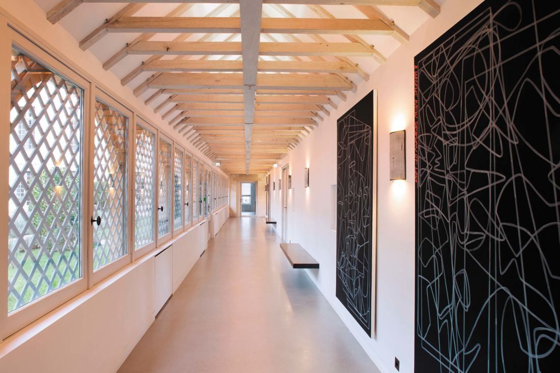 Kering: Long corridor under a timber roof with lattice windows on one side and large dark artworks on the other