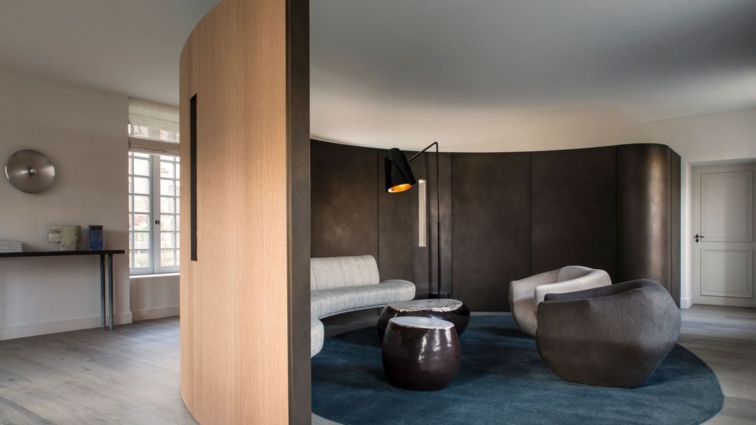 Kering: Lounge with a curved bronze-coloured wall, pale curved sofa, dark sculptural tables and an oak partition