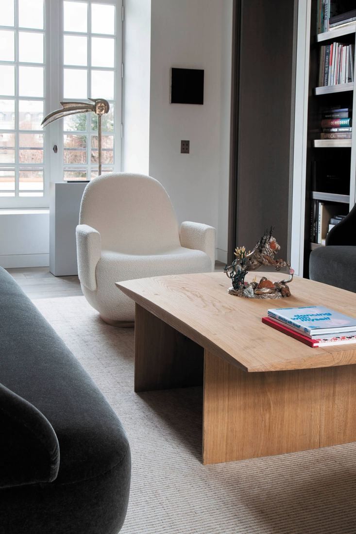 Kering: Sitting area with a cream armchair, low oak table and bookshelves by a window