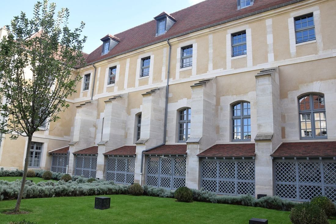 Kering: Stone facade with lattice screens along the ground floor beside a lawn