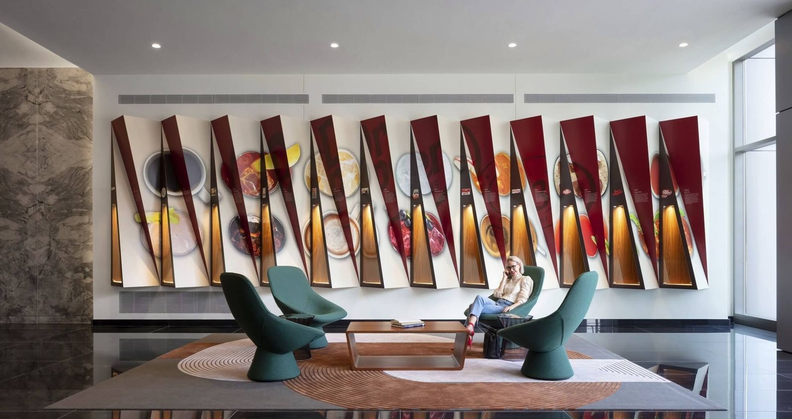 Keurig Dr Pepper: A lounge with green chairs in front of a wall of angled red panels lit from within