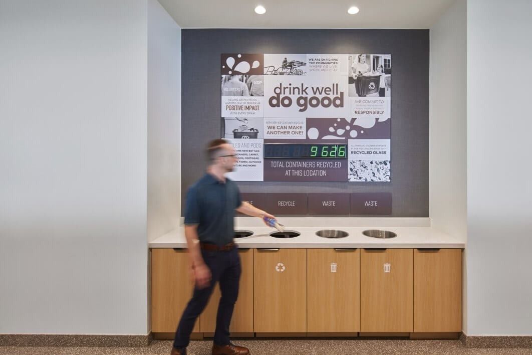 Keurig Dr Pepper: A man dropping waste into recycling bins below a sign reading drink well do good
