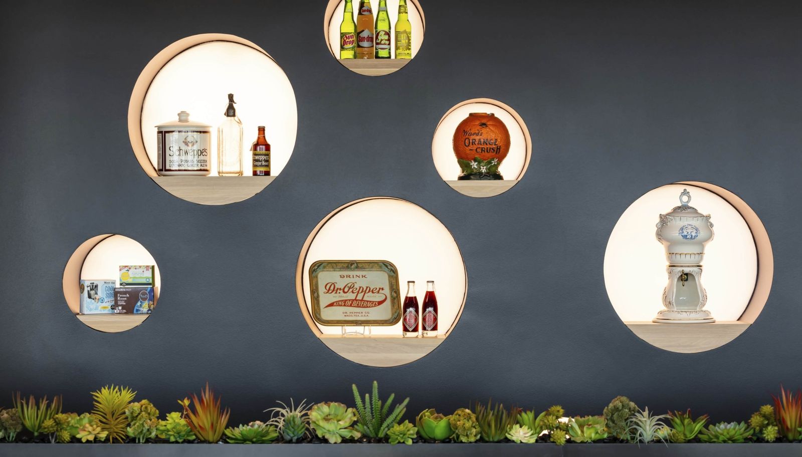 Keurig Dr Pepper: Round niches on a dark wall holding old bottles, signs and a soda dispenser