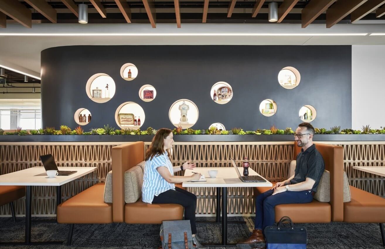 Keurig Dr Pepper: Two people working in an orange leather booth below round display niches