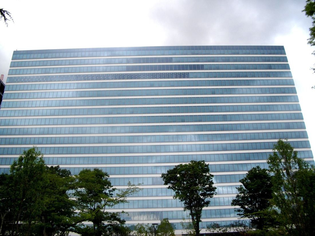 Kirin Holdings: Broad glass facade of a tower seen from below with trees in front