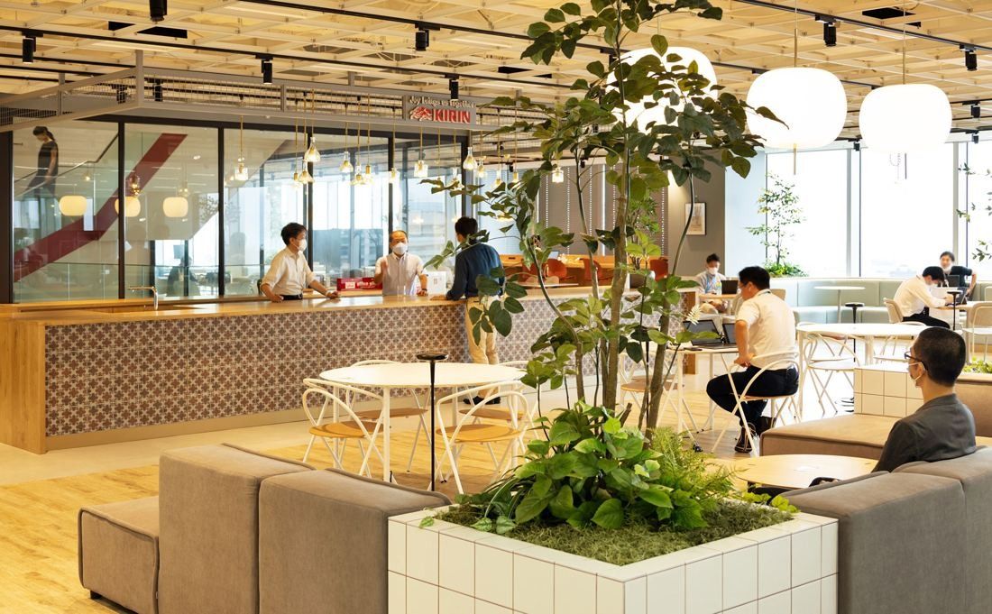 Kirin Holdings: Café counter with patterned tiles, white tables and a large planter in a bright lounge