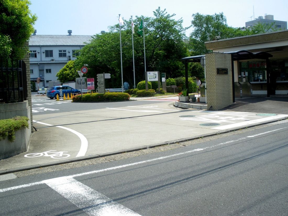 Entrance road and gatehouse of a brewery site with an older building behind trees
