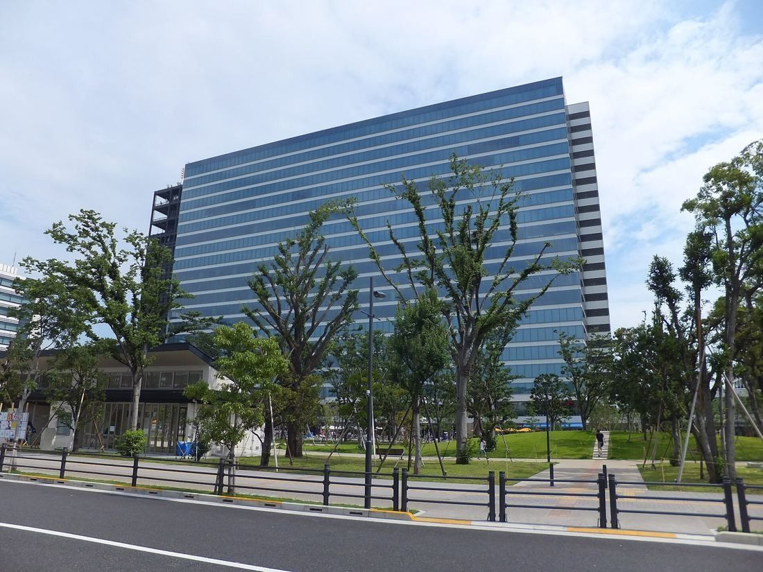 Kirin Holdings: Glass office tower behind young trees along a road