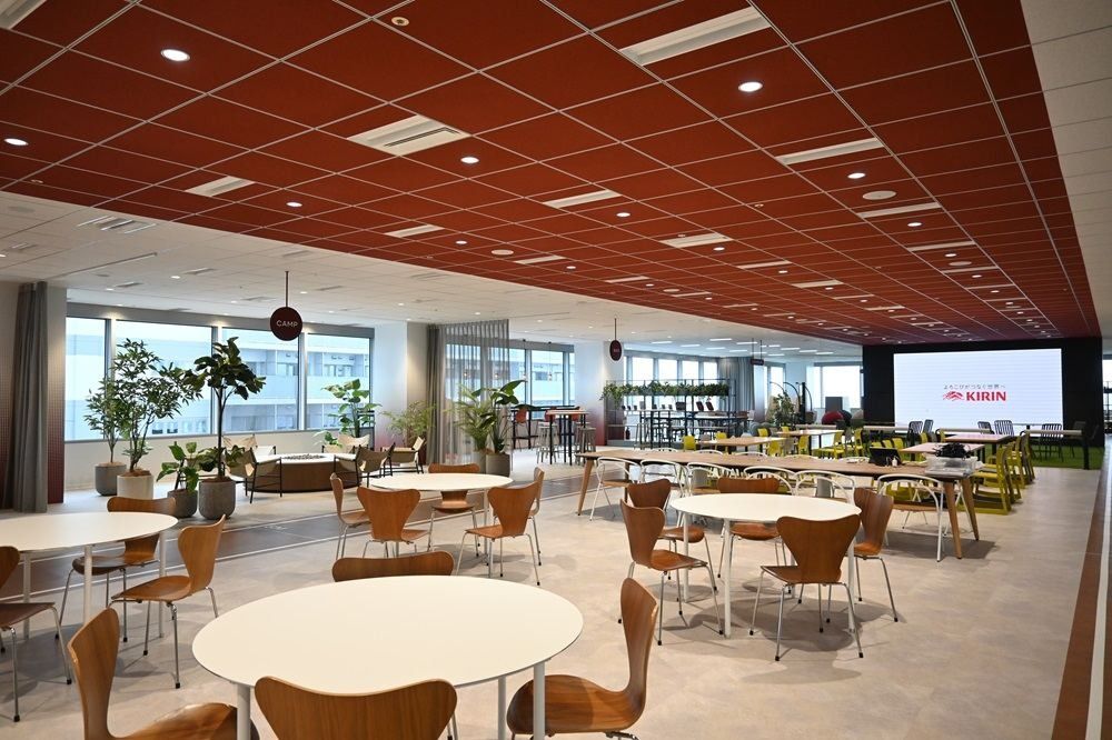 Kirin Holdings: Large lounge with round white tables, wooden chairs and a terracotta ceiling beside tall windows