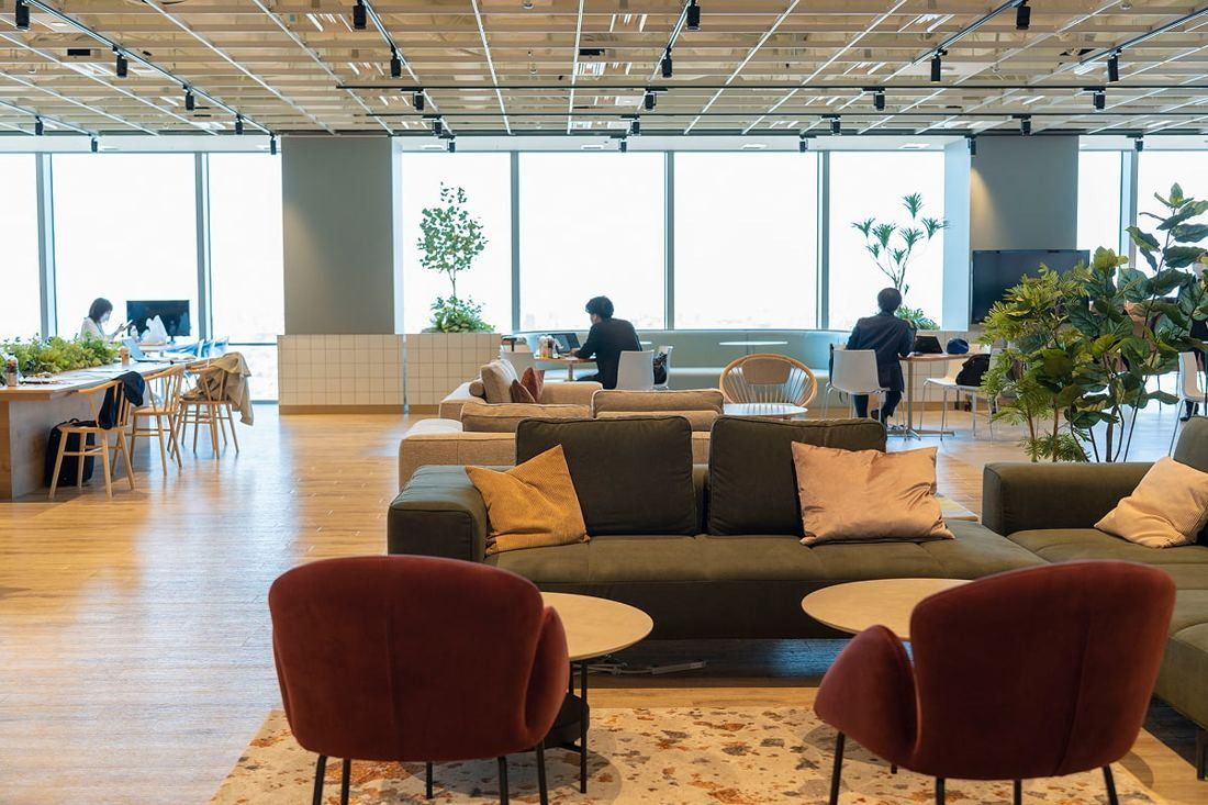 Kirin Holdings: Lounge with a dark sofa, red armchairs and round tables on wooden flooring