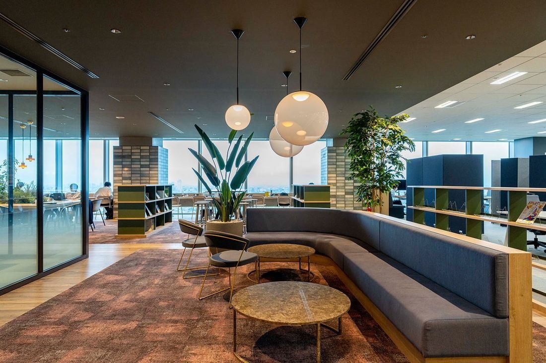 Kirin Holdings: Lounge with a long grey sofa, round tables and globe pendant lamps among bookshelves