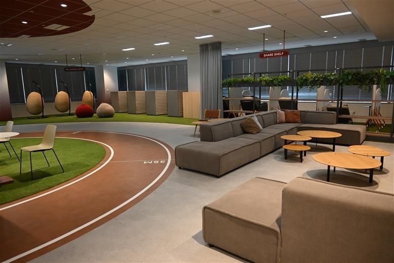 Kirin Holdings: Lounge with sofas and round tables beside a strip of artificial grass and a running-track floor