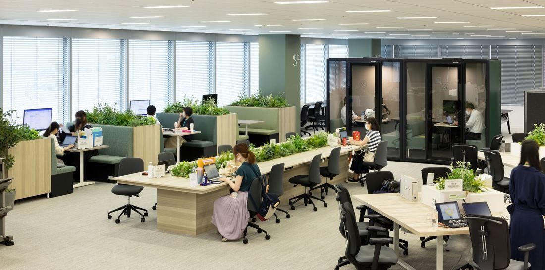 Kirin Holdings: Open office with sit-stand desks, planters along the desks and glass booths at the back