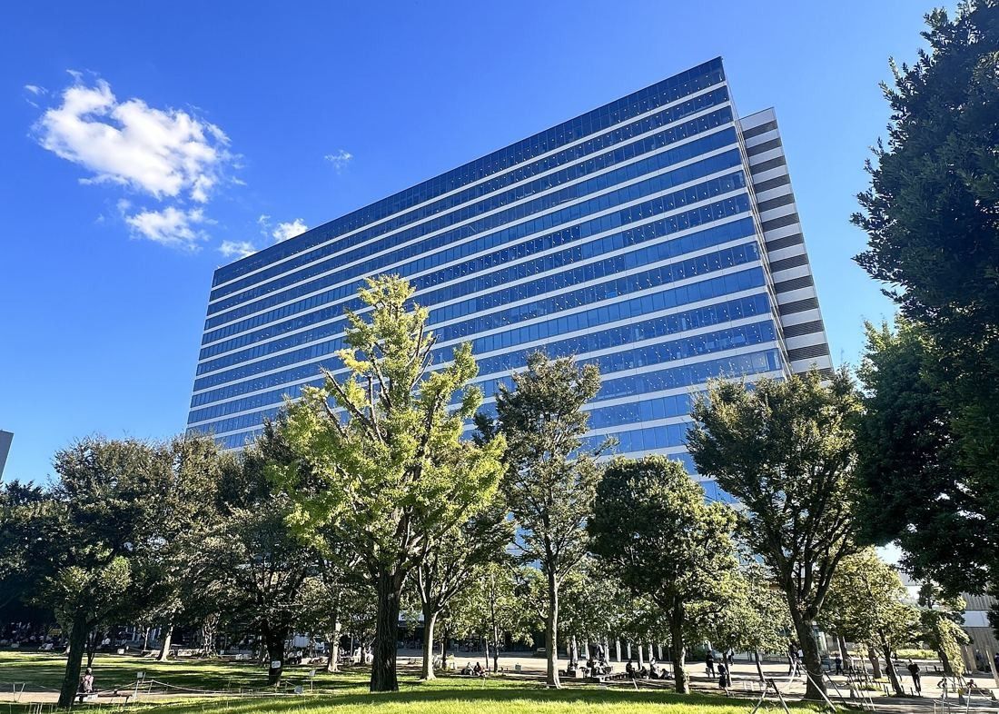 Kirin Holdings: Tall glass office tower rising behind a row of leafy trees under a blue sky