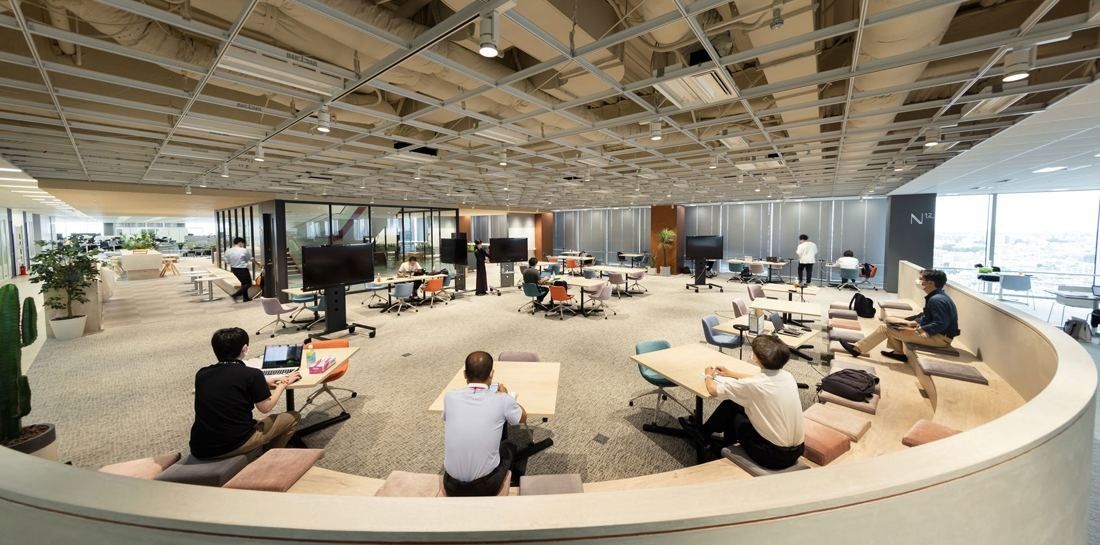 Wide open-plan floor with a curved, sunken tiered seating area in the middle and desks around it
