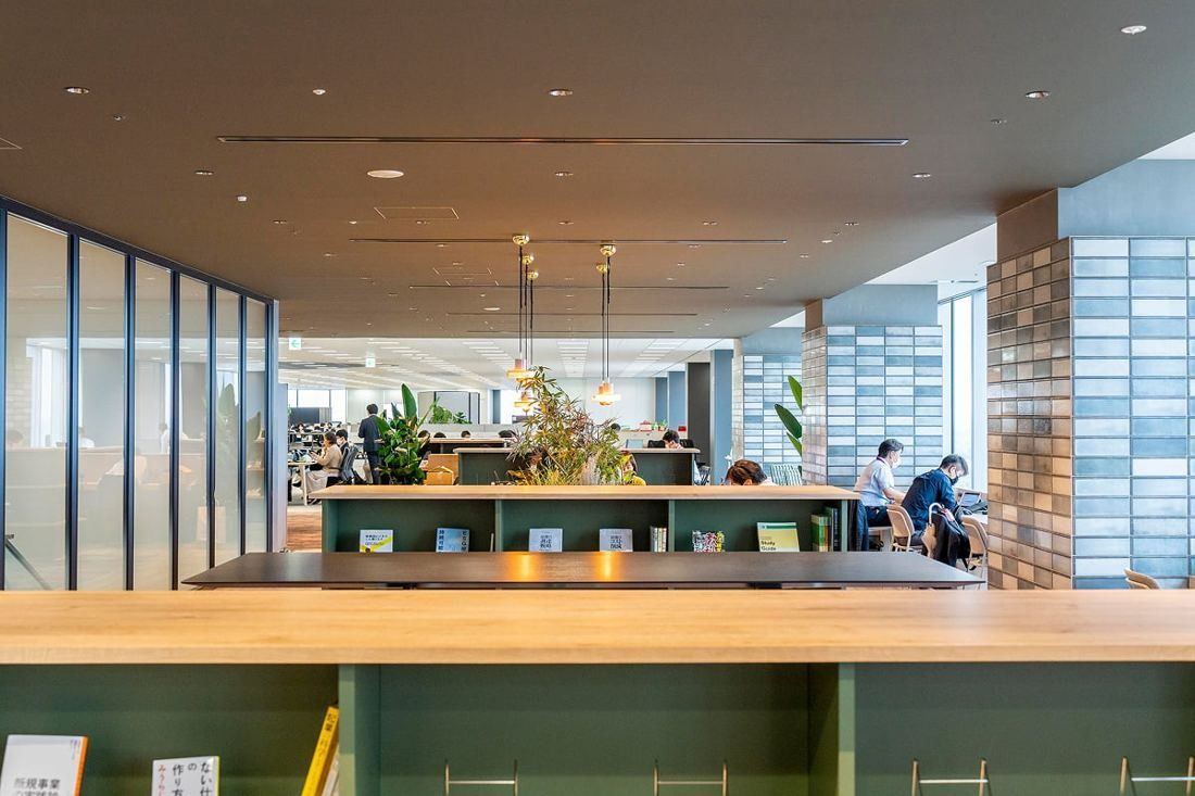 Kirin Holdings: Wooden counter and bookshelves with plants in a long library space