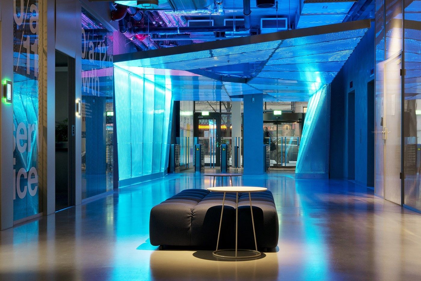 Klarna: Blue-lit lobby with angled perforated panels and a round black bench