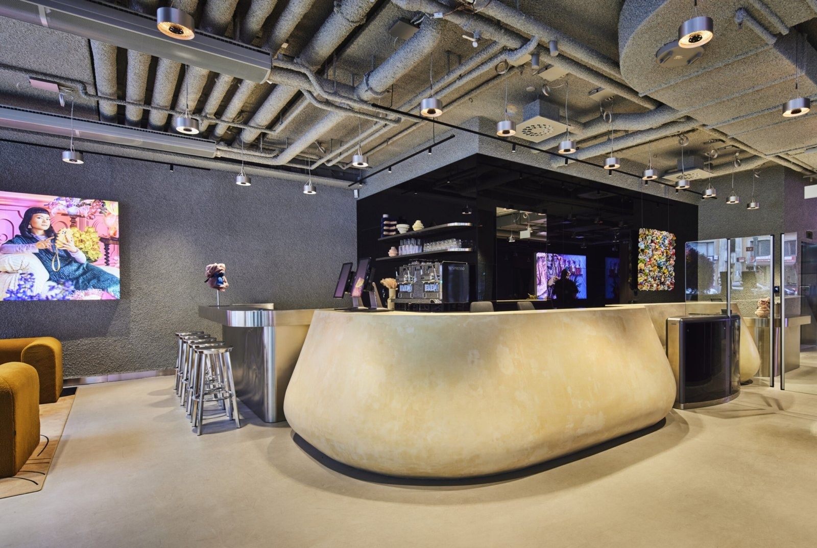 Klarna: Curved cream-coloured bar counter under exposed ceiling ducts, with screens and a black box structure behind