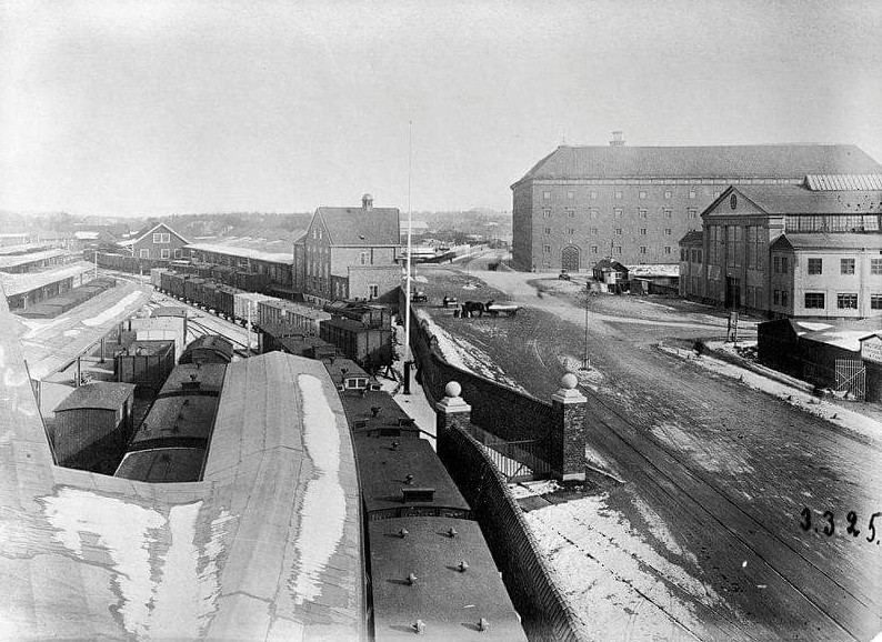 Black-and-white view east along Norra Stationsgatan with railway yards and large brick buildings