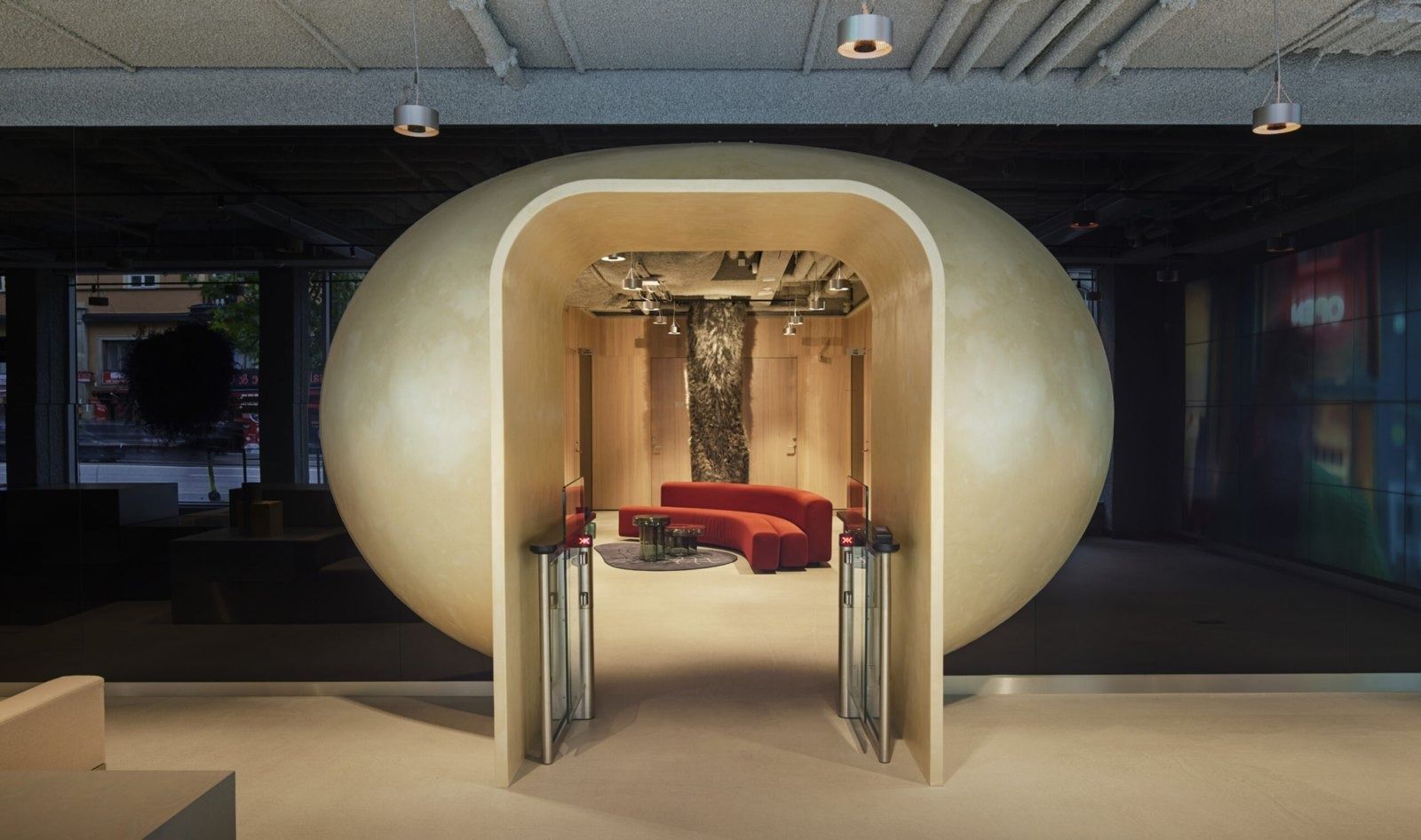 Klarna: Large egg-shaped pale wooden portal opening onto a small lounge with red sofa
