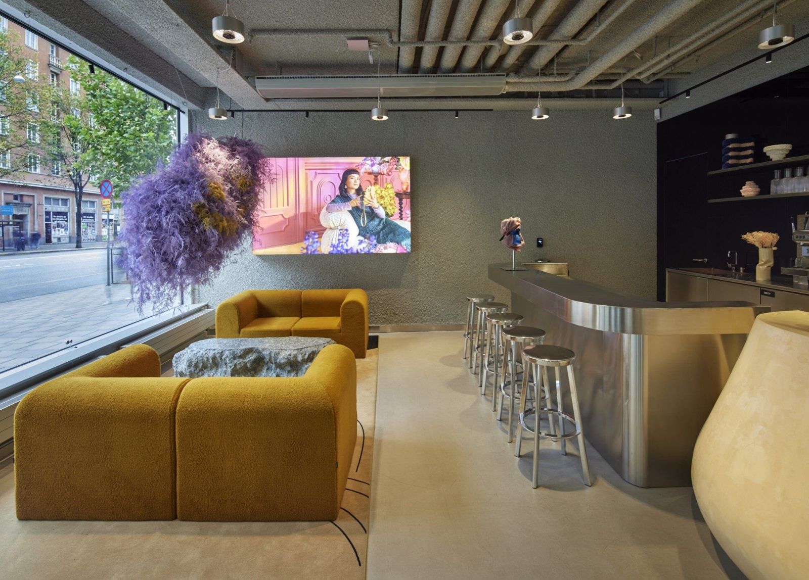 Klarna: Ochre sofas and a steel bar with stools beside a street window and a purple hanging installation