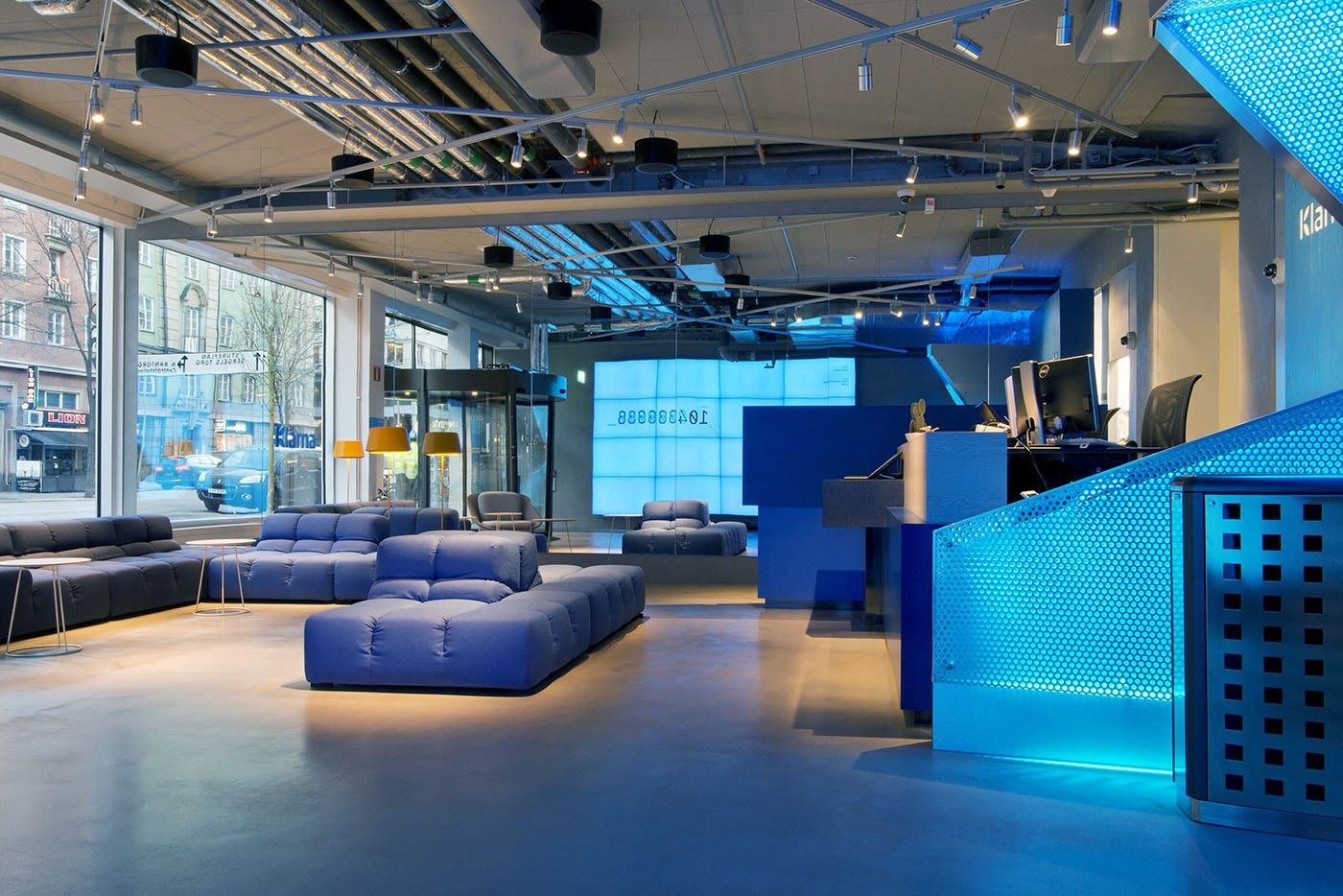 Klarna: Open lounge with blue modular sofas, a blue counter and windows onto the street