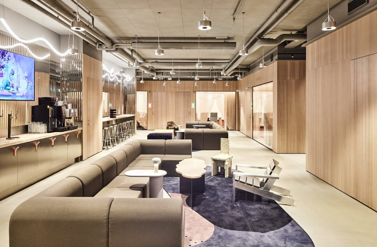 Klarna: Open pantry and lounge with wood-clad walls, long grey sofa and a purple rug