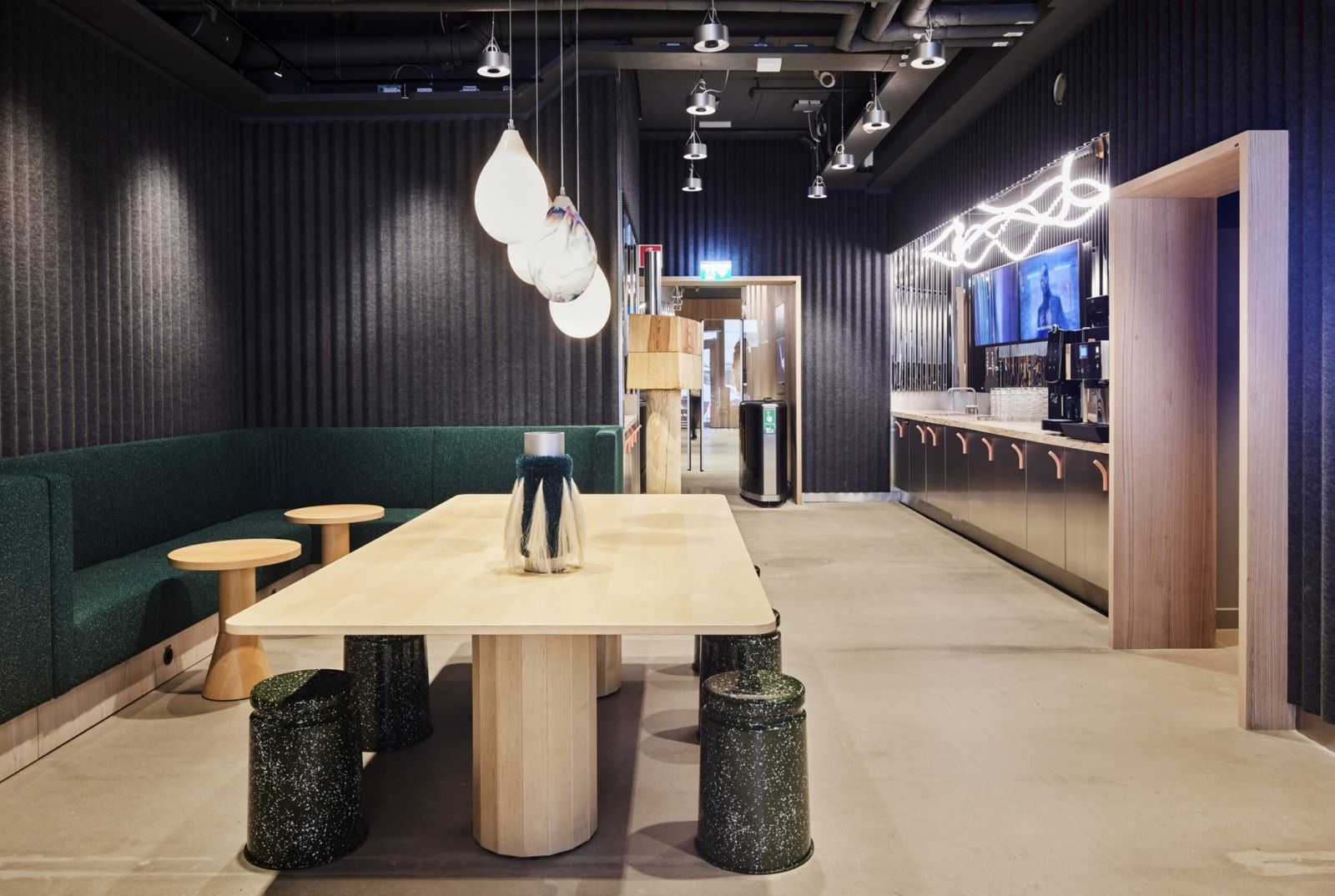 Klarna: Pantry with a pale wooden table, dark green booth seating, pendant lamps and a coffee counter