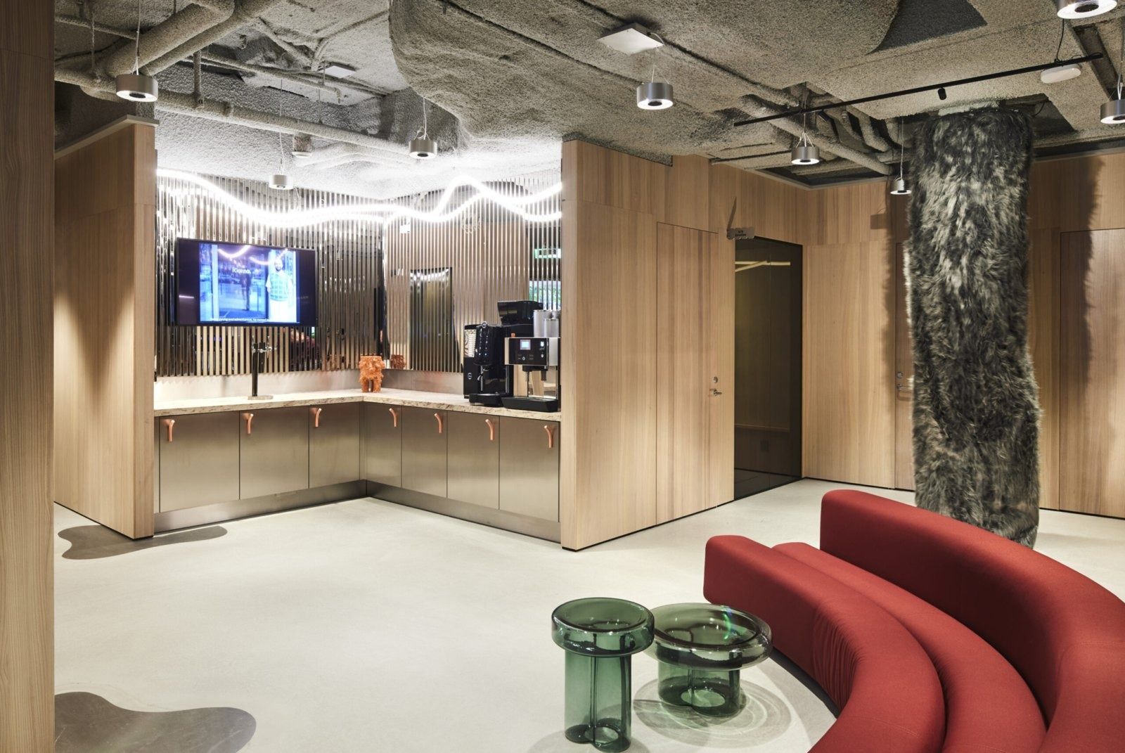 Klarna: Pantry with wooden cabinets, coffee machines, a rough stone column and a red curved sofa