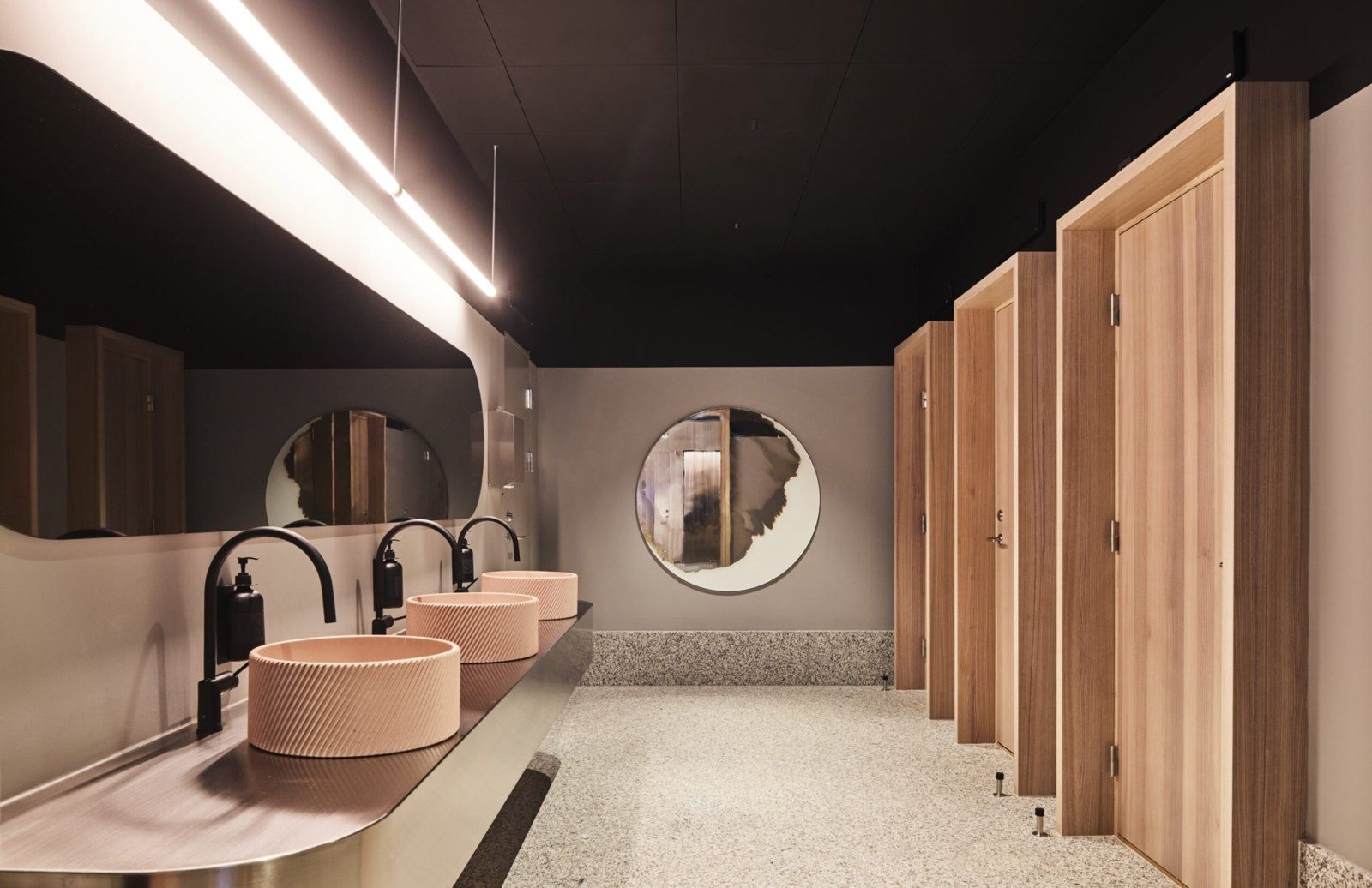 Klarna: Washroom with pink round basins, round mirrors and dark wooden stall doors