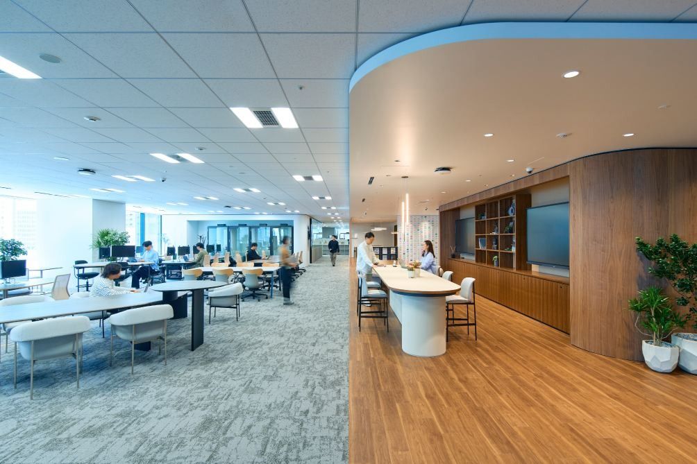 KOKUYO: Bright office floor with long shared tables, a curved wooden wall and planters