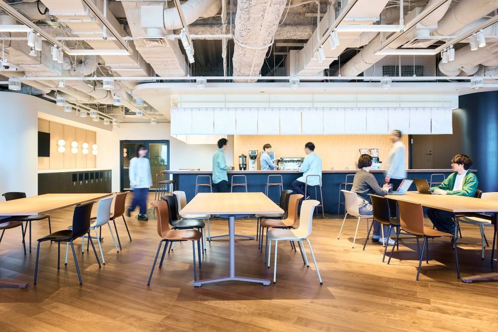 KOKUYO: Café with wooden tables and chairs in front of a counter with coffee machines