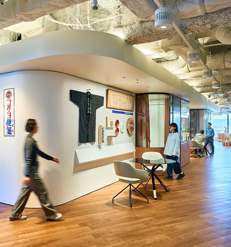 KOKUYO: Curved white wall with historic items and a vertical sign, a person walking past