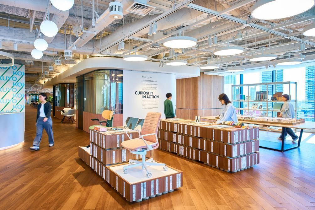 KOKUYO: Display tables made of stacked boxes holding chairs and products under round ceiling lights