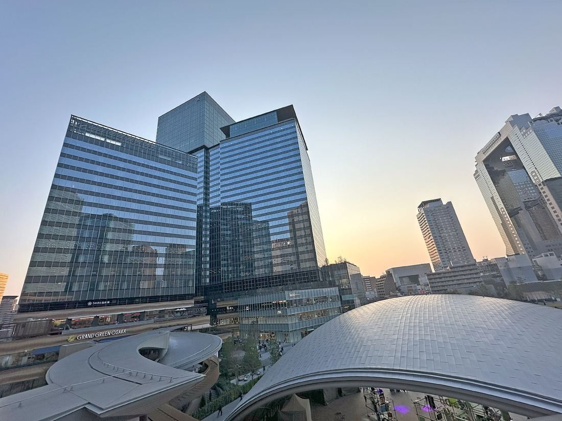 KOKUYO: Glass towers at dusk with a curved metal roof in the foreground