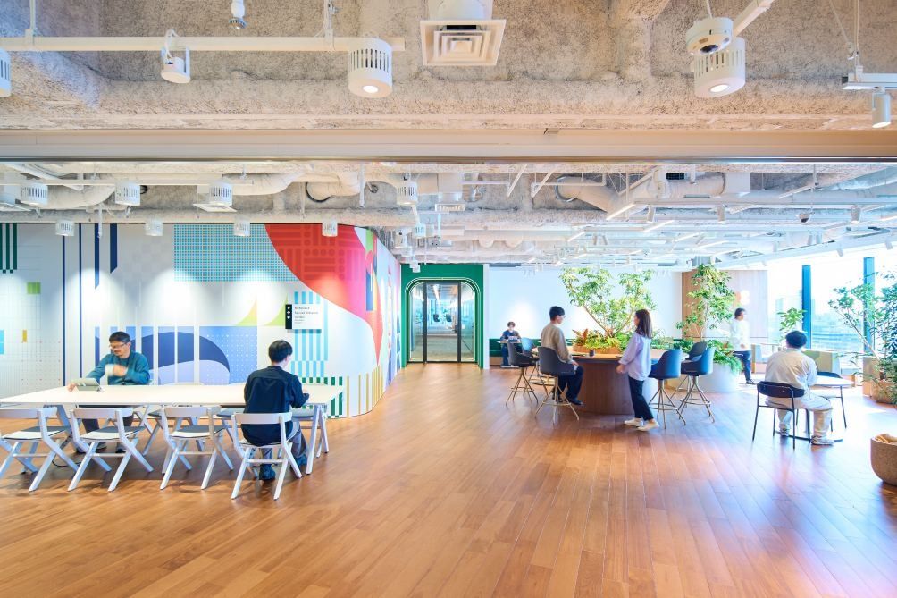 KOKUYO: Large open area with a colourful tiled mural, white tables and plants