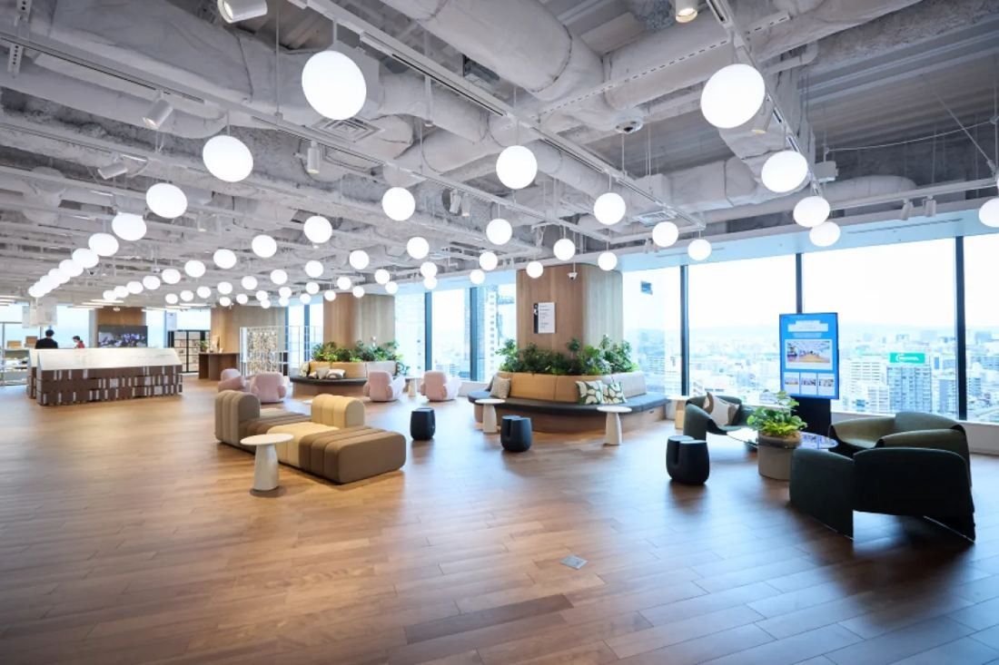 KOKUYO: Open lounge with sofas, plants and rows of round pendant lights beside tall windows