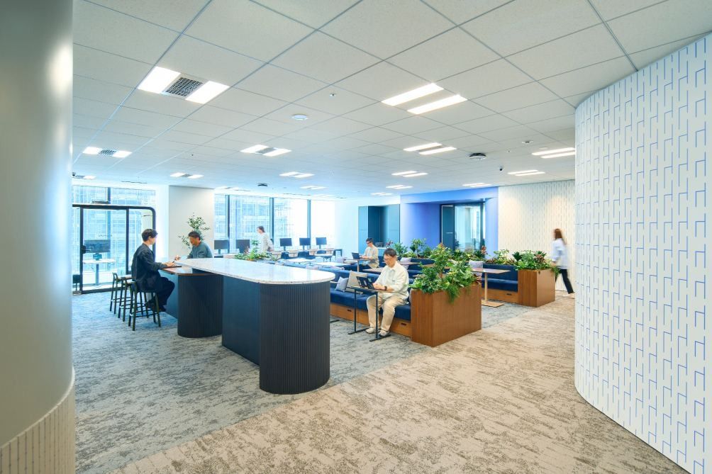 KOKUYO: Open work area with a dark island table, sofas and a white textured partition